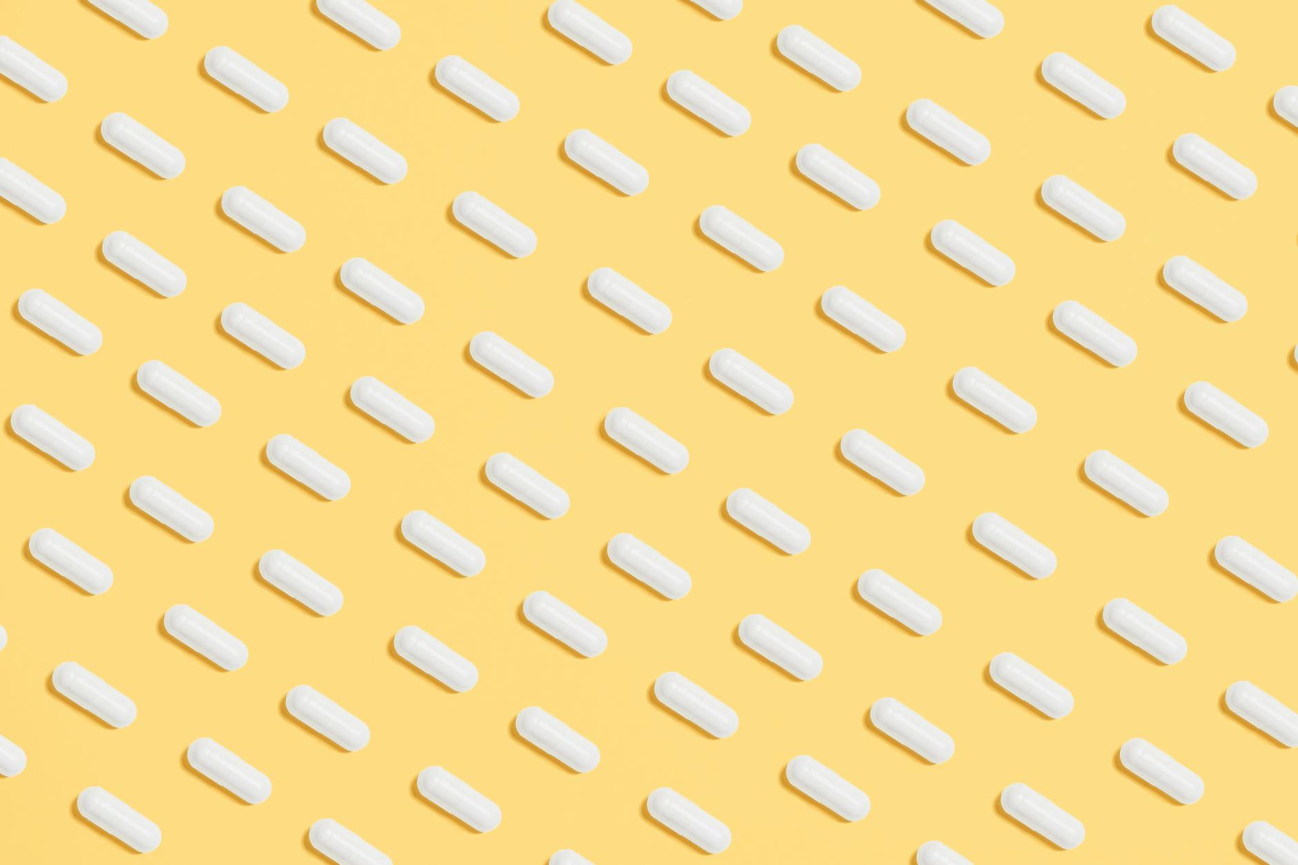 Pattern of white capsules on a bright yellow surface, symbolizing healthcare and medicine.