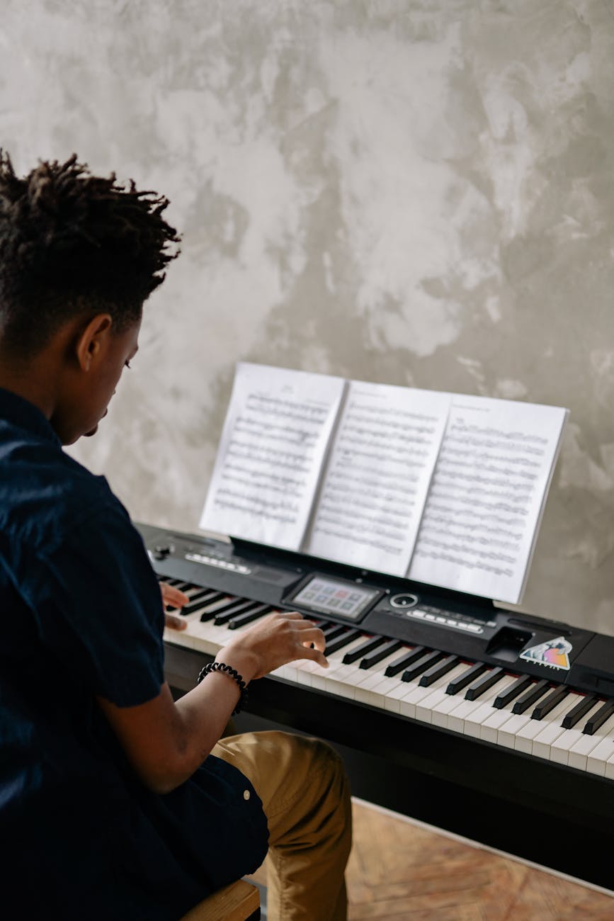 A young boy focused on playing the piano while reading sheet music. Indoor setting.