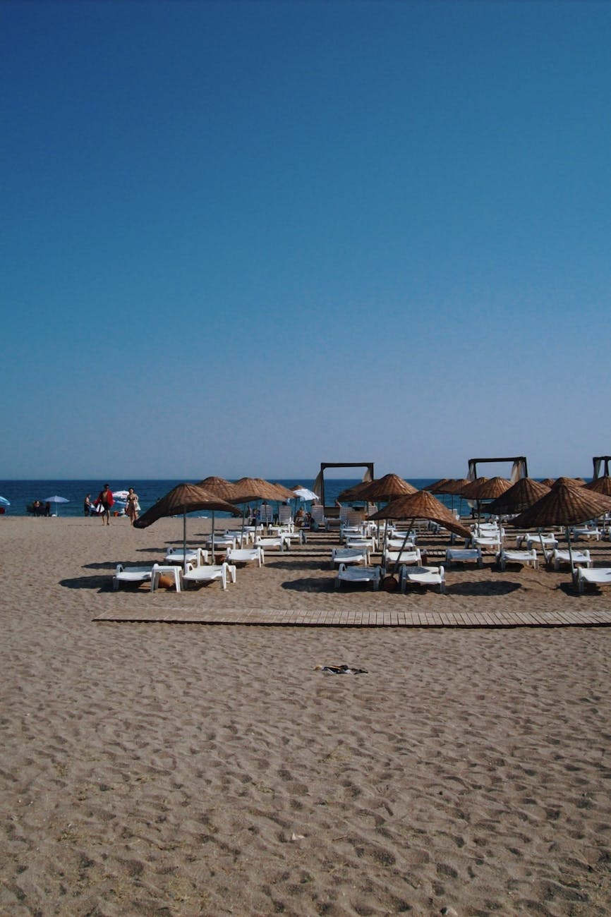 A scenic summer beach with straw umbrellas and loungers under a clear blue sky.