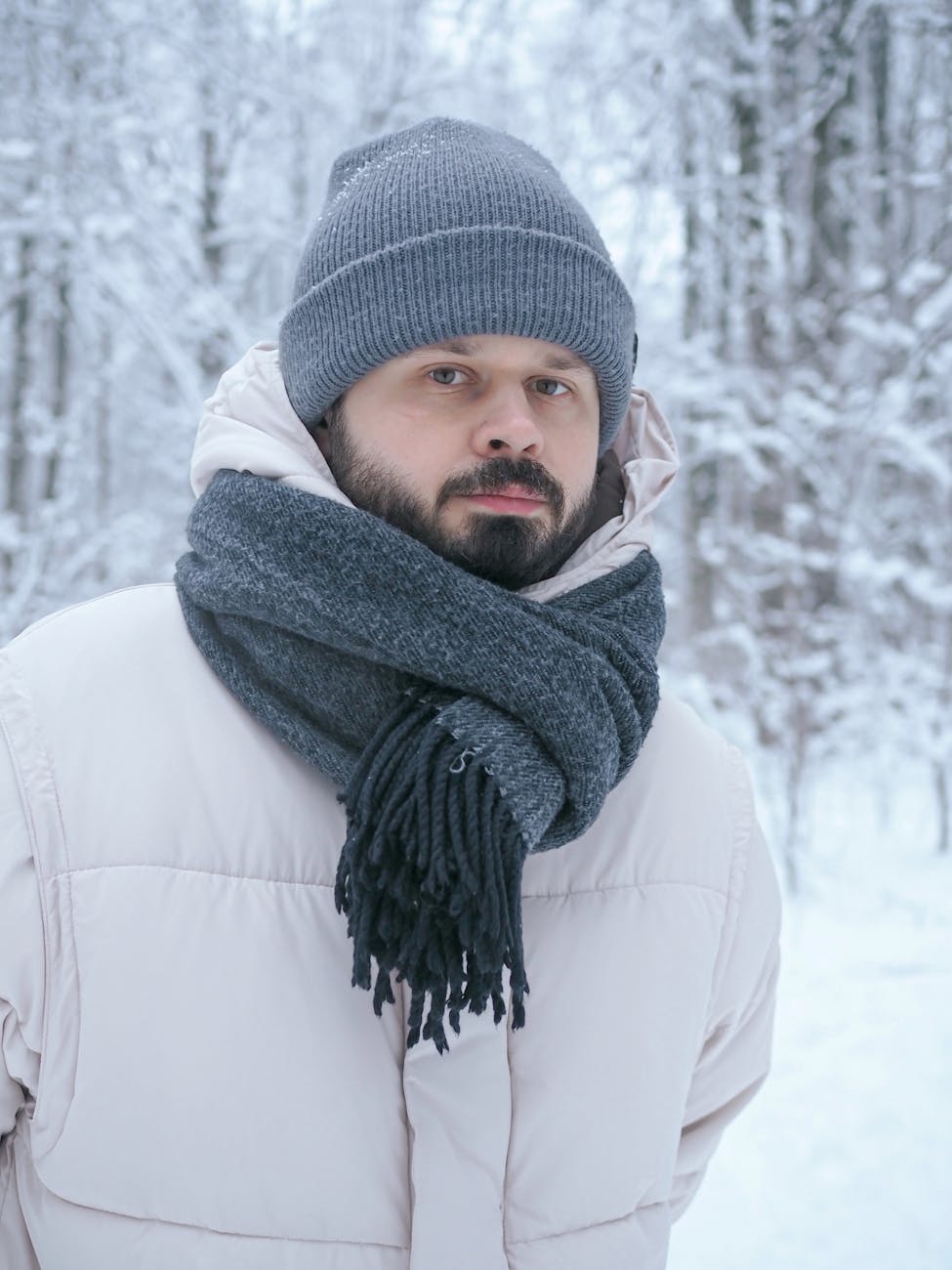 Portrait of a bearded man wearing winter clothes in a snowy forest, showcasing stylish winter fashion.