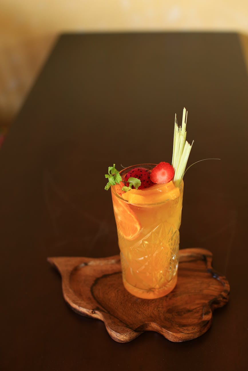 A vibrant tropical drink in Hoi An, Vietnam, featuring orange slices and lemongrass garnish, served on a wooden platter.