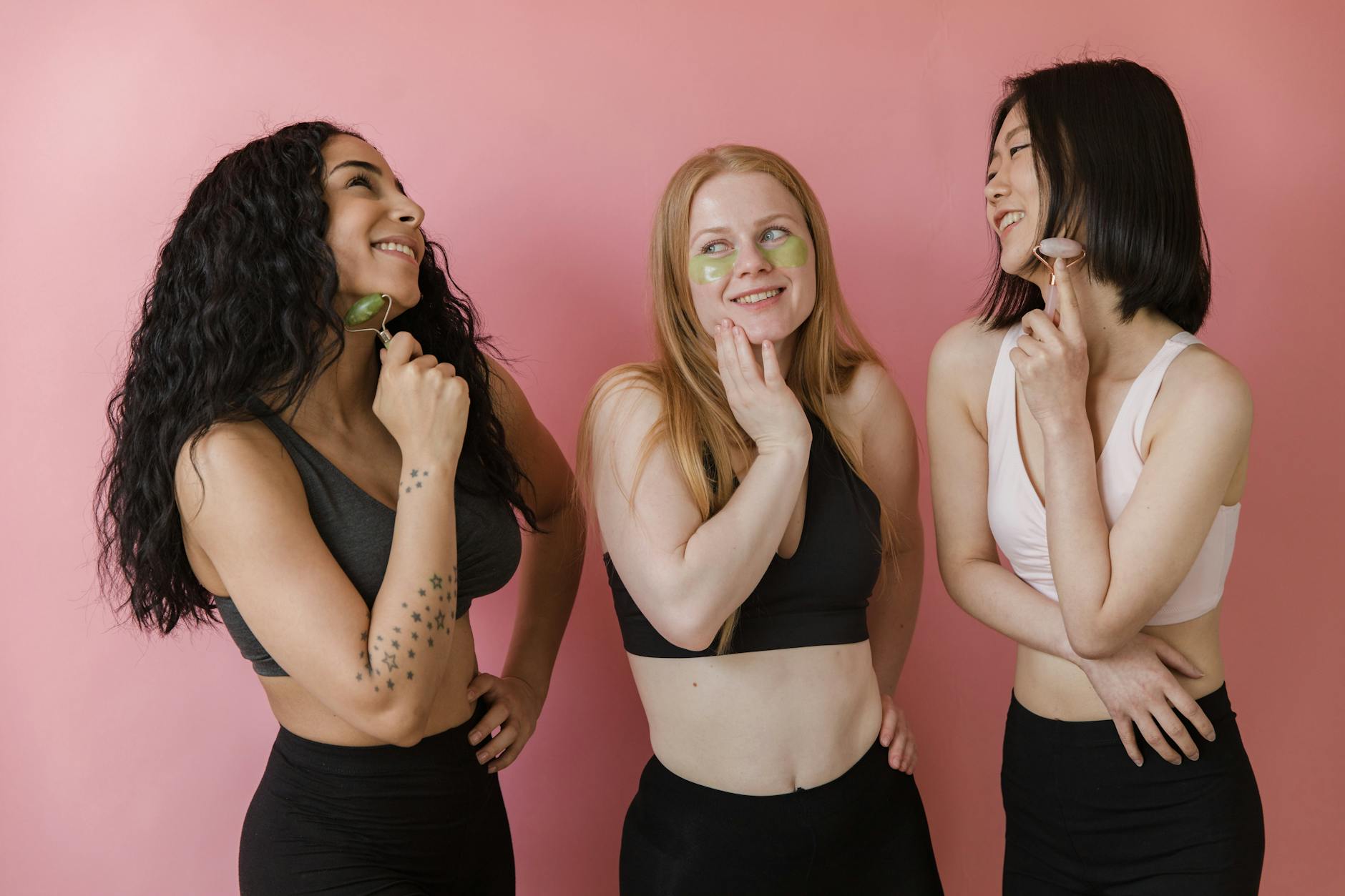 Three diverse women using jade rollers and face masks, enjoying a skincare routine.
