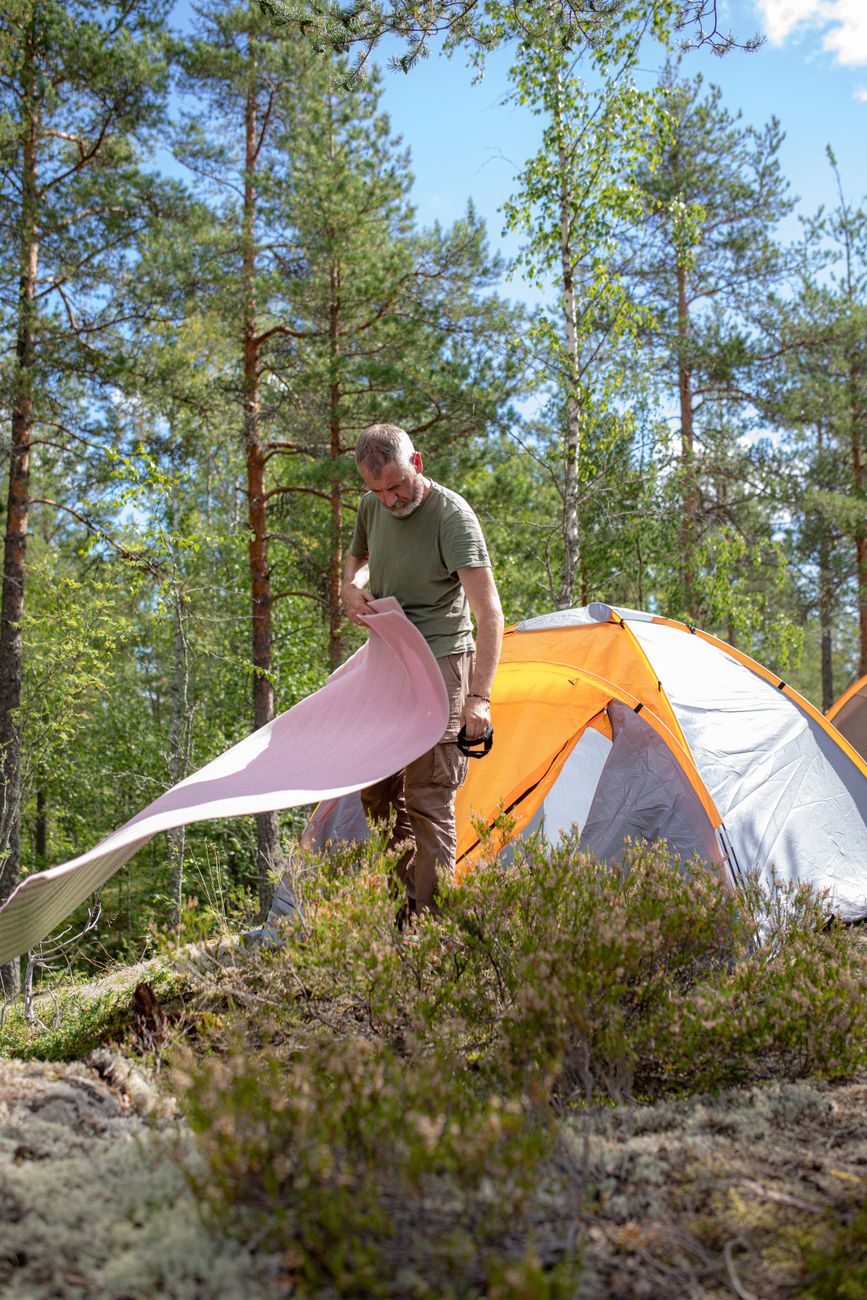 A man preparing camping gear near a tent in a sunlit forest setting.