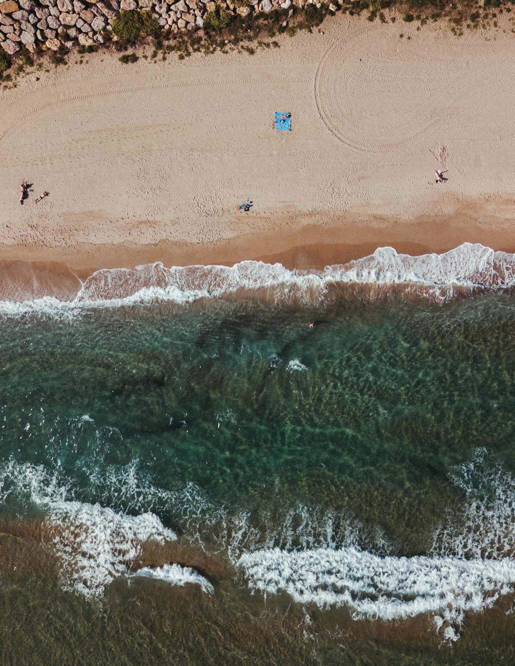 Drone shot capturing the picturesque beach in Barcelona with clear waves and scattered beachgoers.