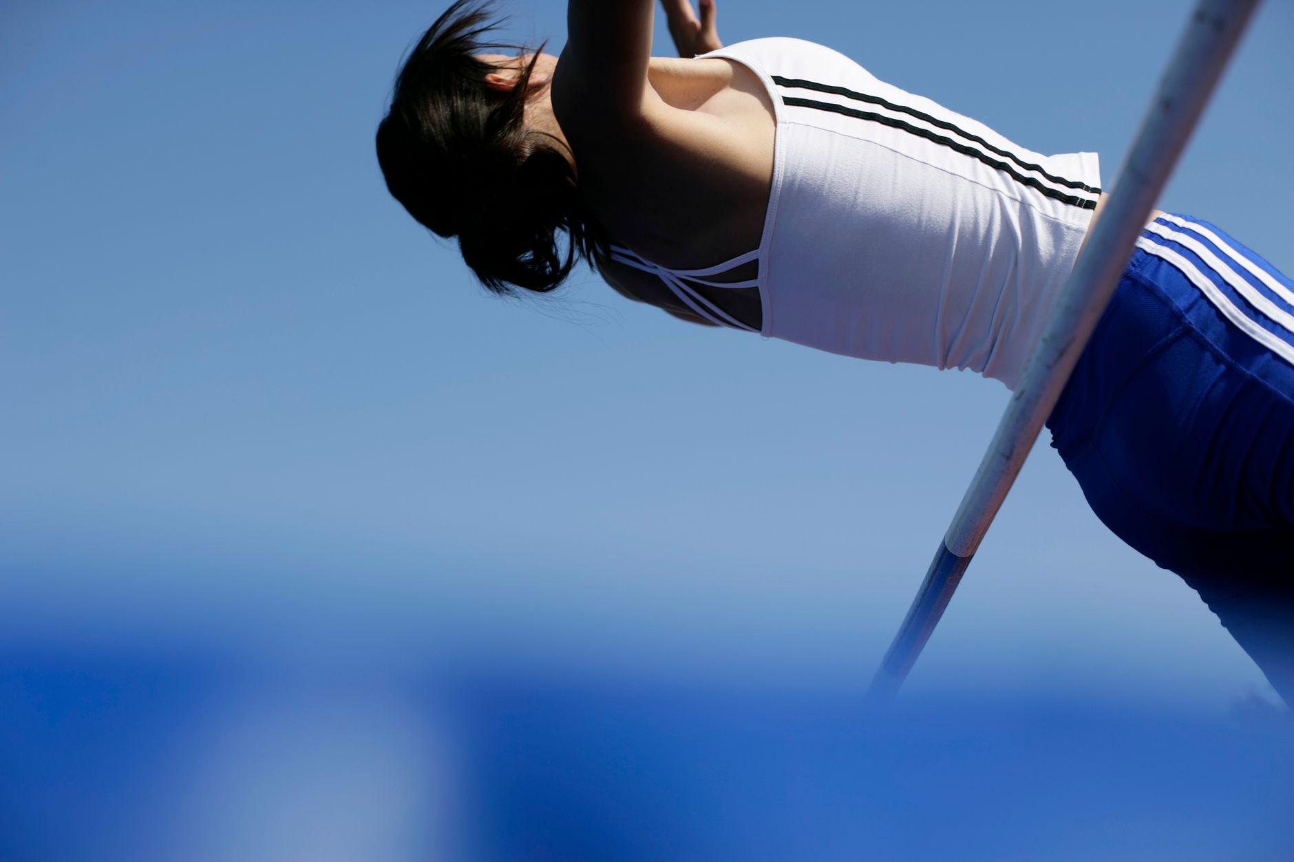 High jump athlete caught in mid-air during a jump under clear blue skies.