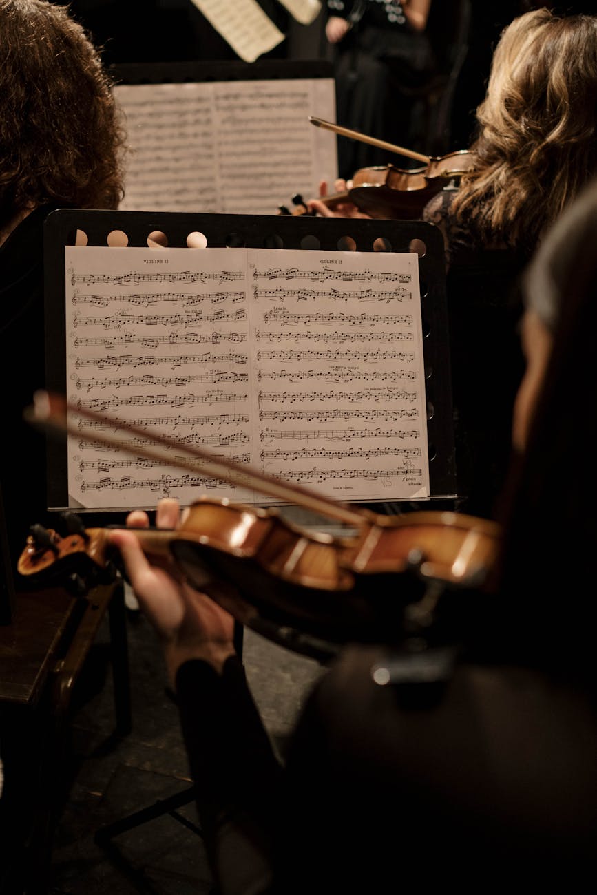 An orchestra violinist during a performance, focusing on sheet music and the instrument.