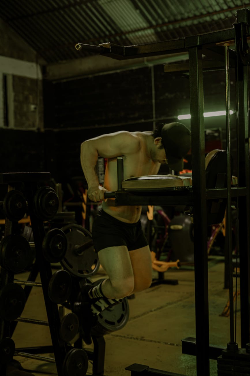 A muscular man performs exercises in a dimly lit gym, showcasing fitness and strength.