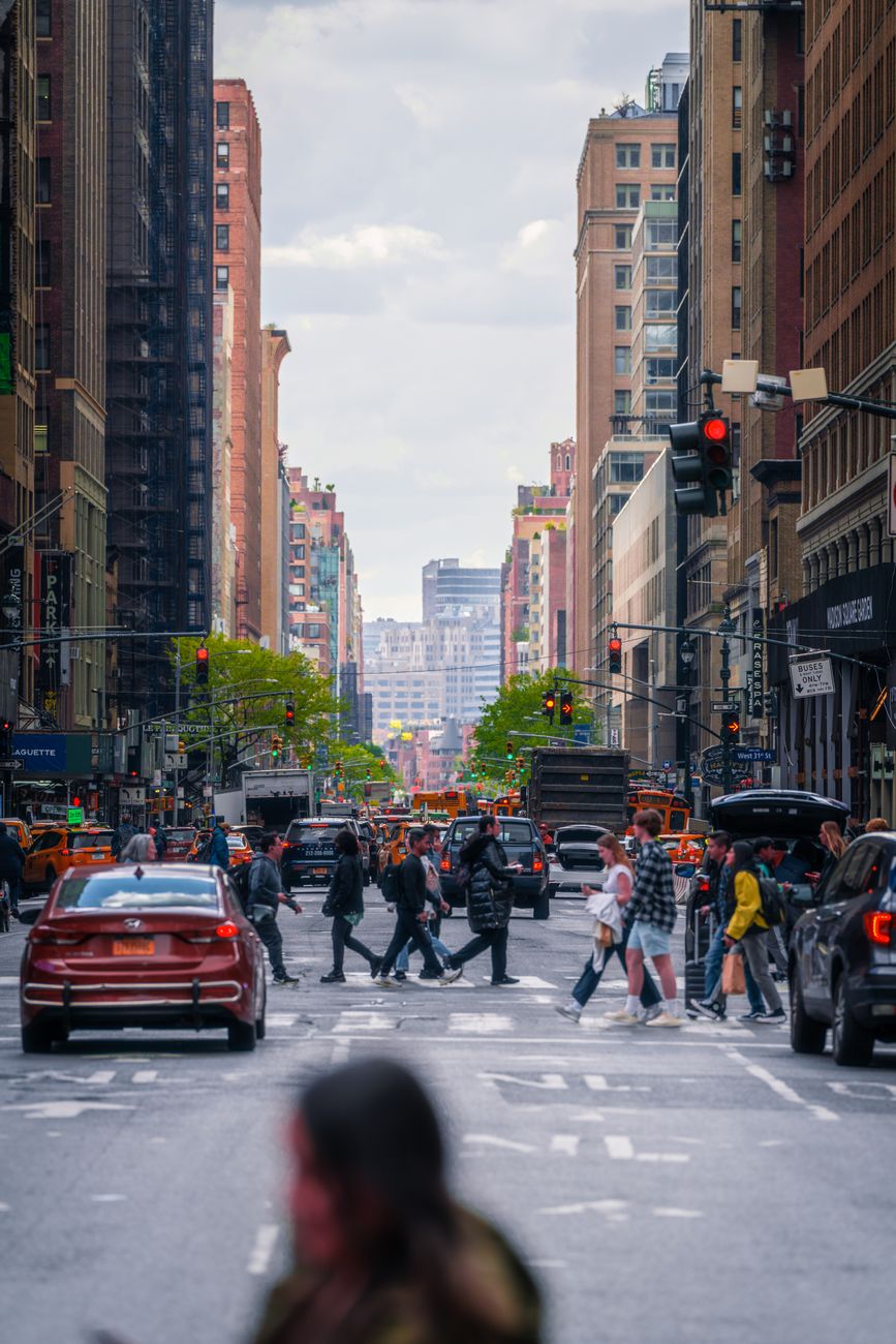 A lively street scene in New York City showcasing pedestrians crossing with iconic urban buildings and traffic.