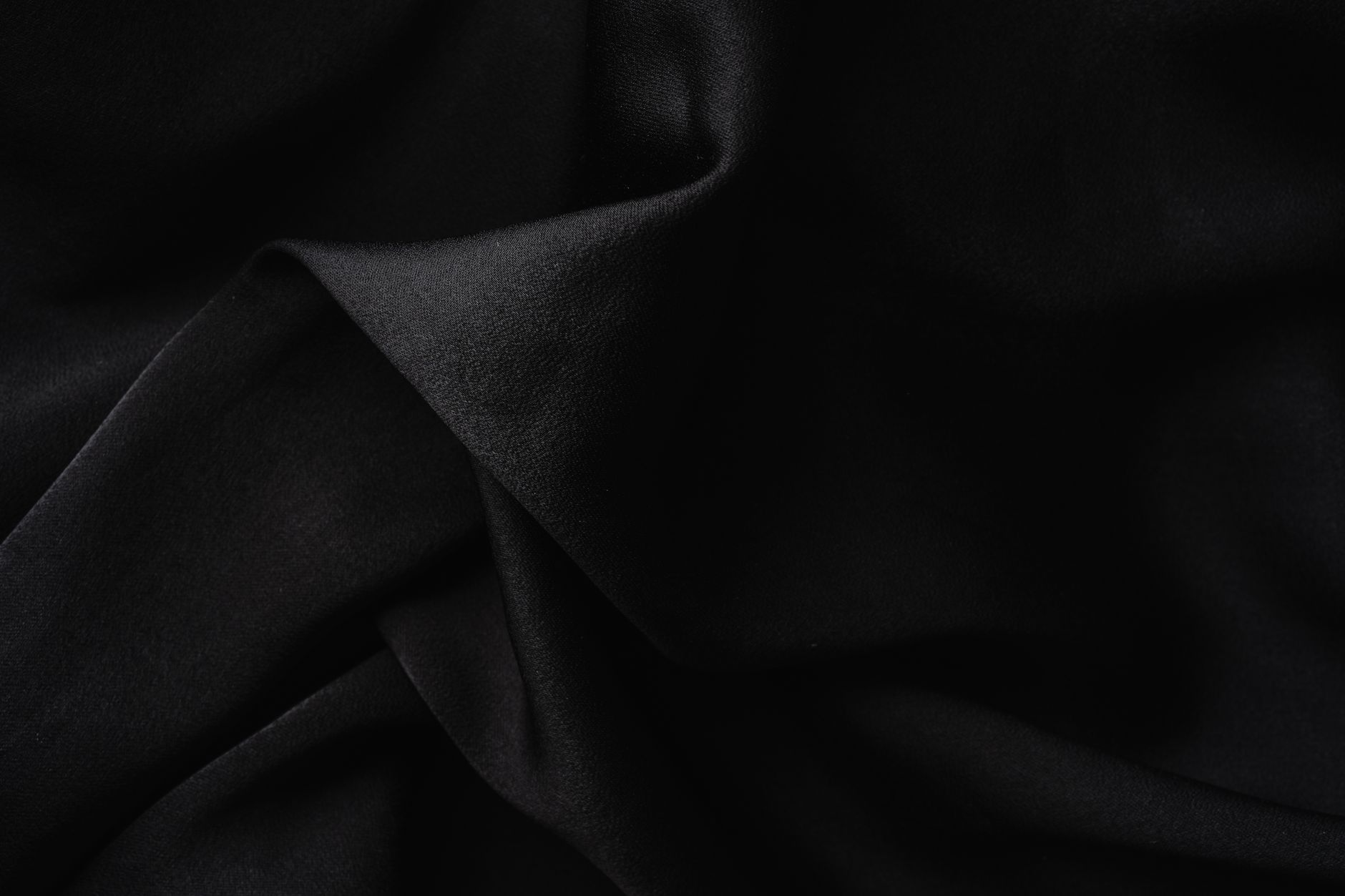 Close-up of luxurious black fabric with soft, elegant folds creating a textured appearance.