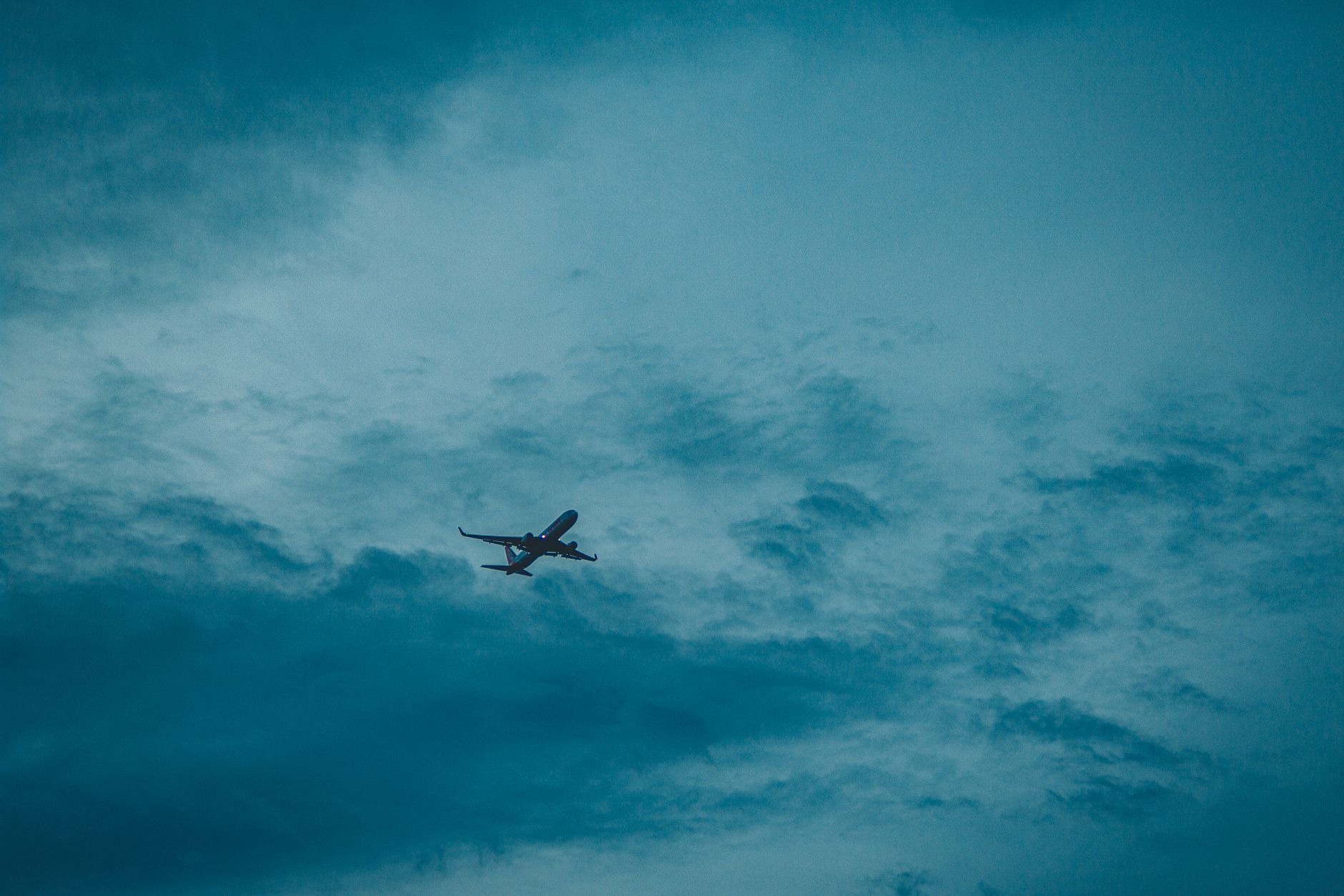 From below of modern airplane flying high in air with clouds at sunset time in nature during flight in evening