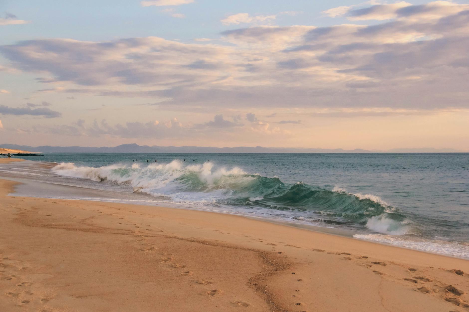 Peaceful beach scene showcasing rolling waves and footprints at sunset on a sandy shore.