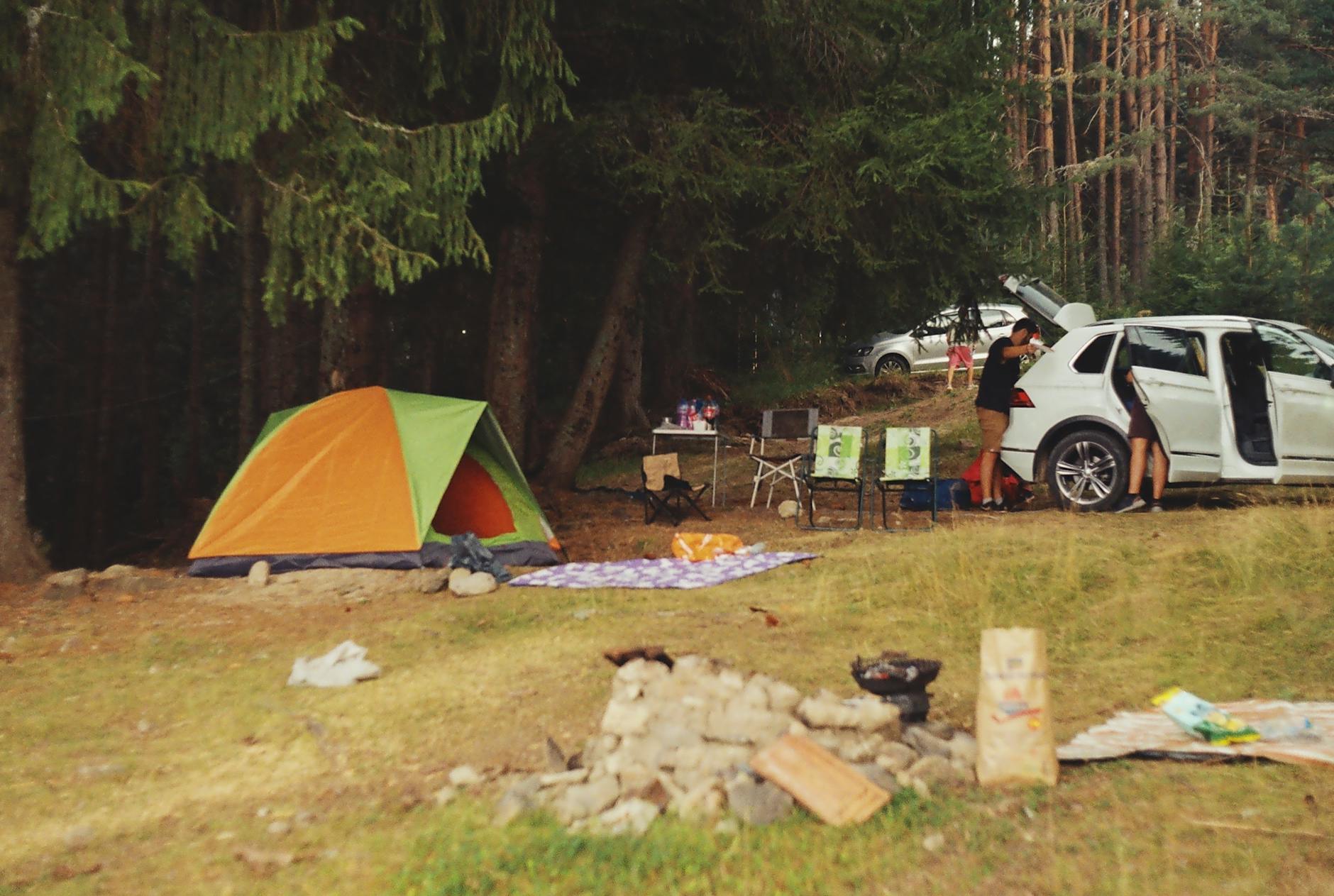 Explore a peaceful camping scene in the forest with a tent, car, and campfire setup.