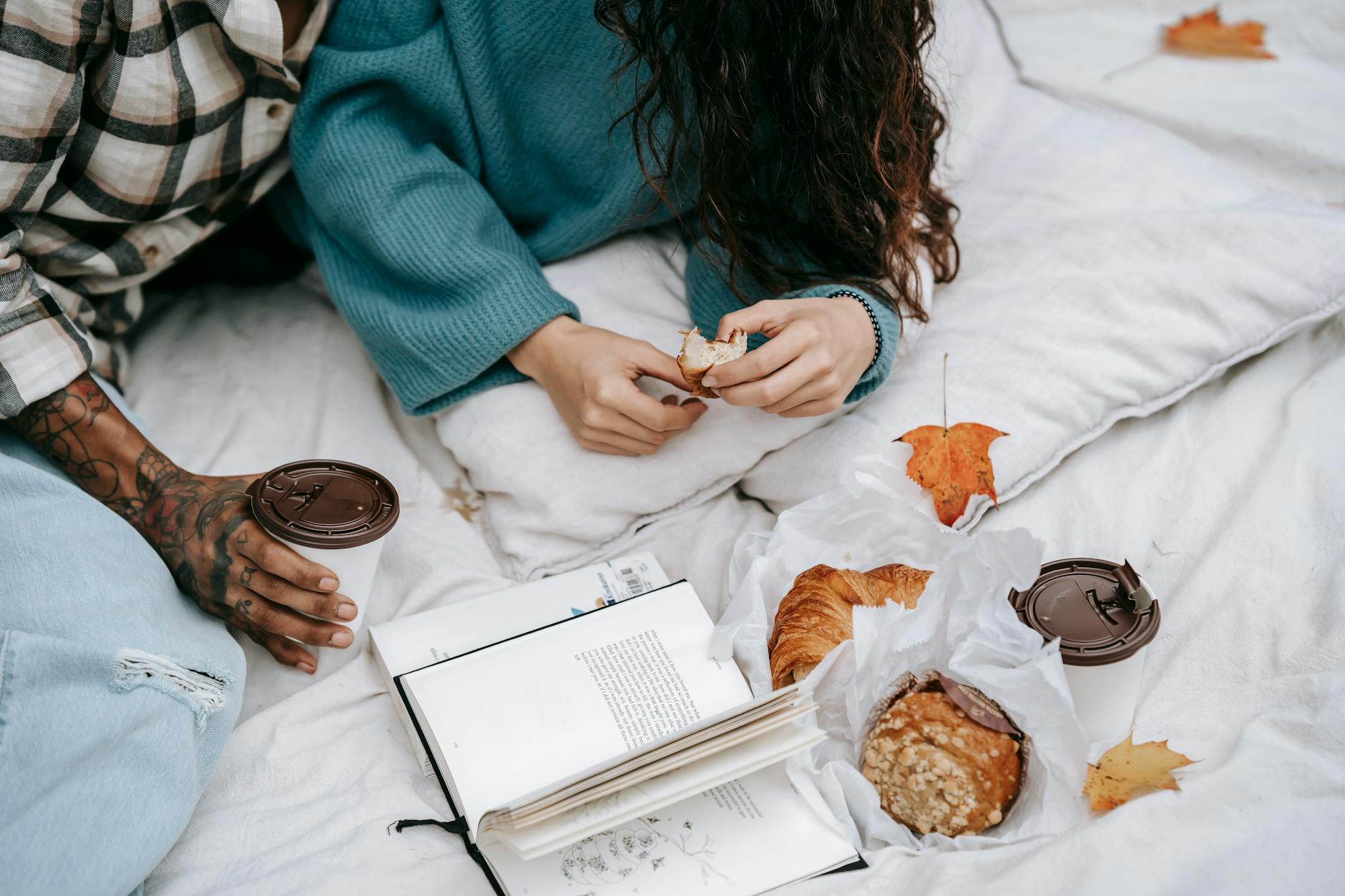 Two people enjoying a relaxed autumn picnic with coffee and pastries on a blanket.
