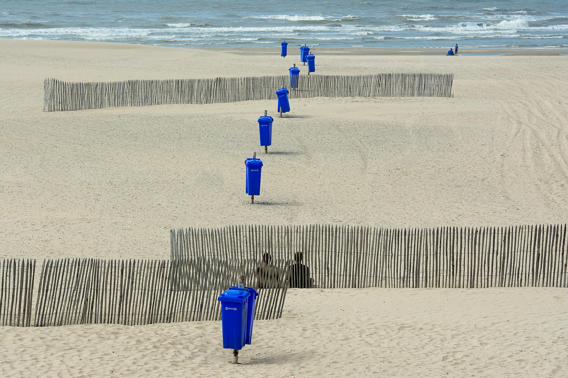 A serene beach scene featuring blue bins and fencing along the sandy shore, ideal for backgrounds.