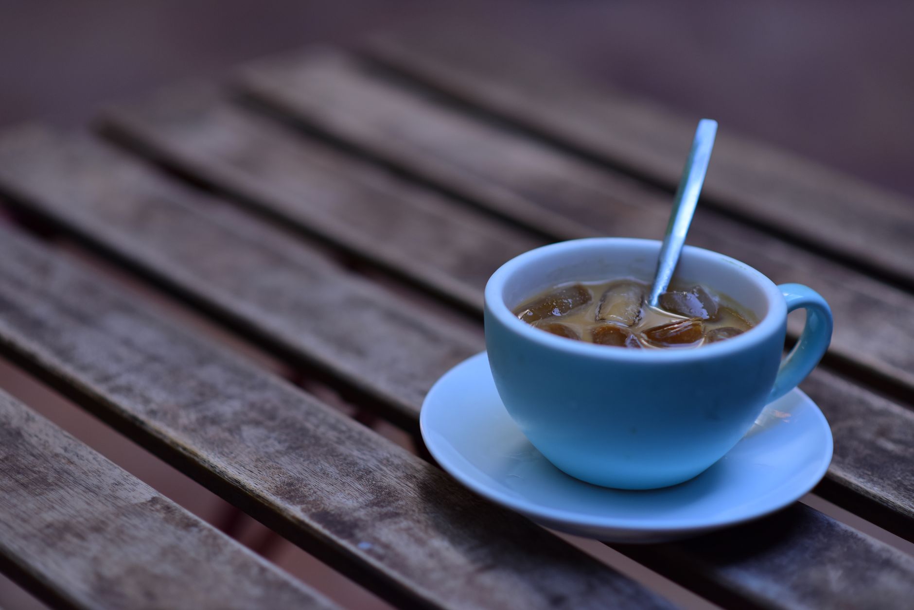 A refreshing iced coffee served in a blue cup on a rustic wooden table, perfect for summer outdoor vibes.