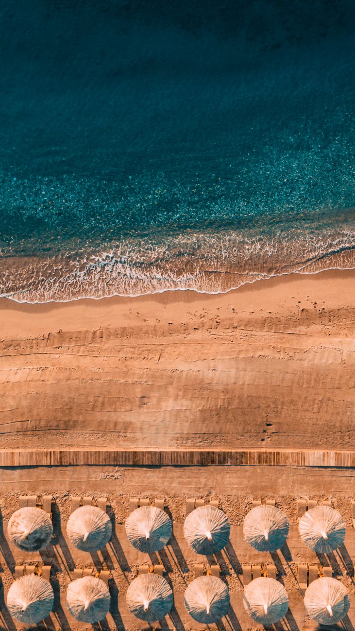 Stunning aerial view of a sandy beach lined with umbrellas alongside a turquoise sea. Perfect for travel and summer themes.