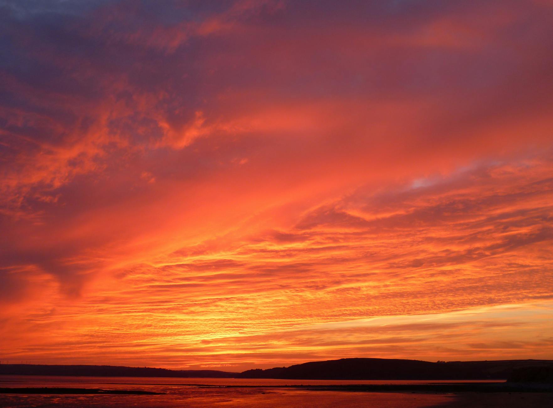 Stunning red sunset with vivid clouds reflecting over tranquil beach waters, capturing nature's beauty.