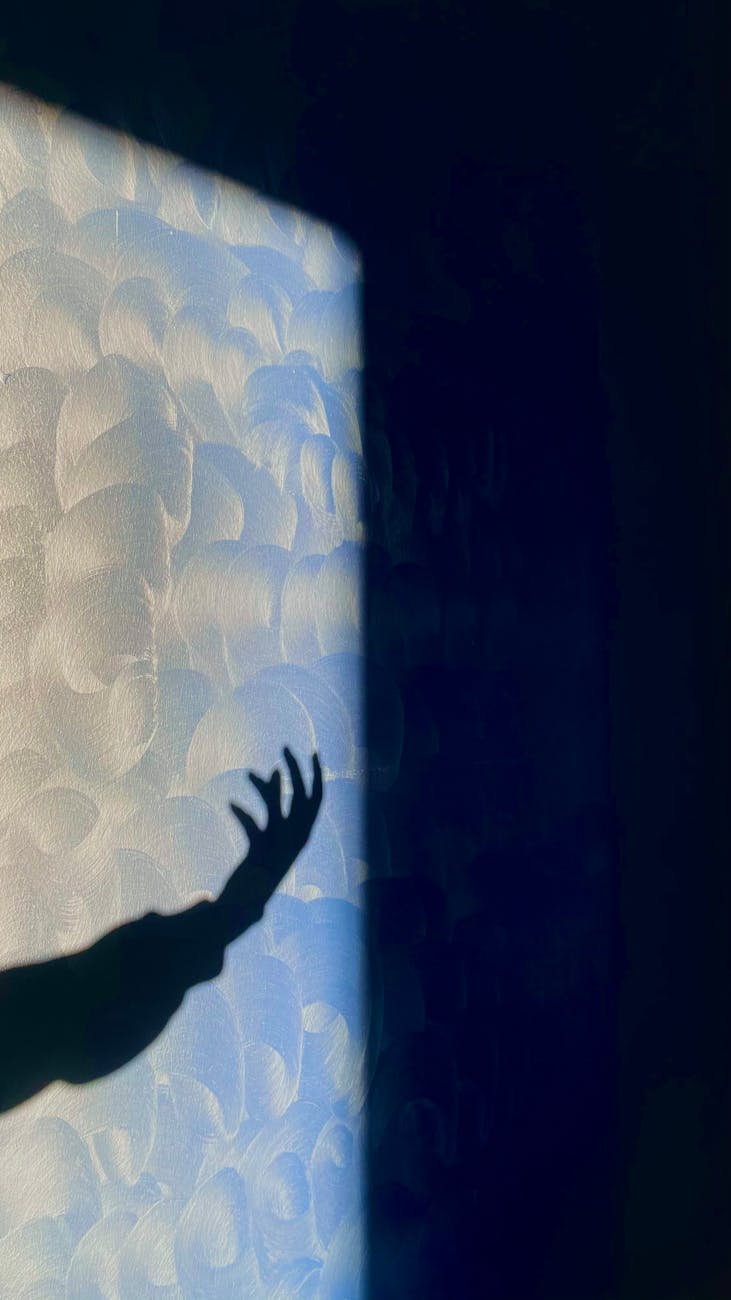 An artistic shadow of a hand reaching on a textured wall with abstract lighting creating a dramatic effect.