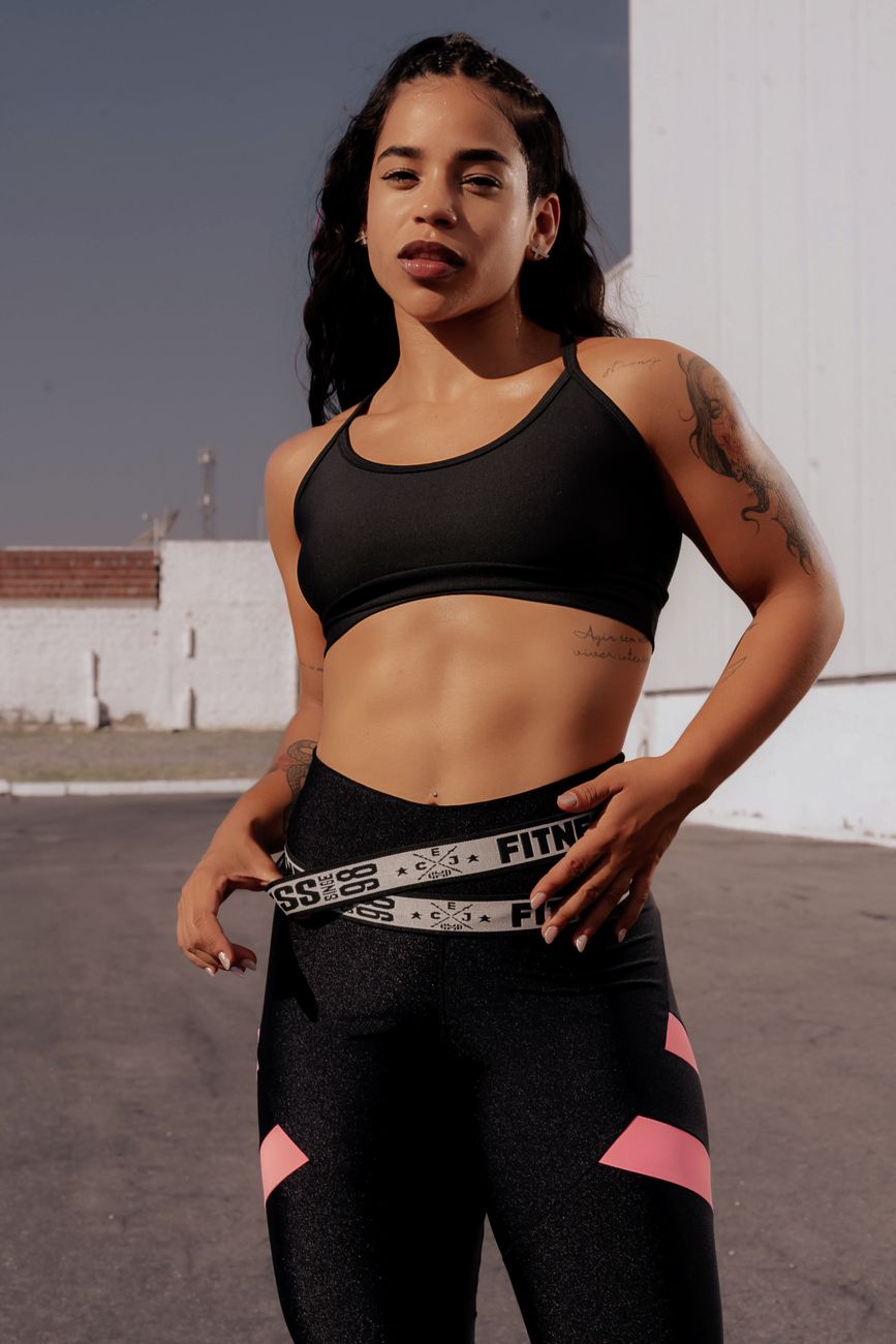 A confident young woman in workout attire posing outdoors. Sunlit and strong.