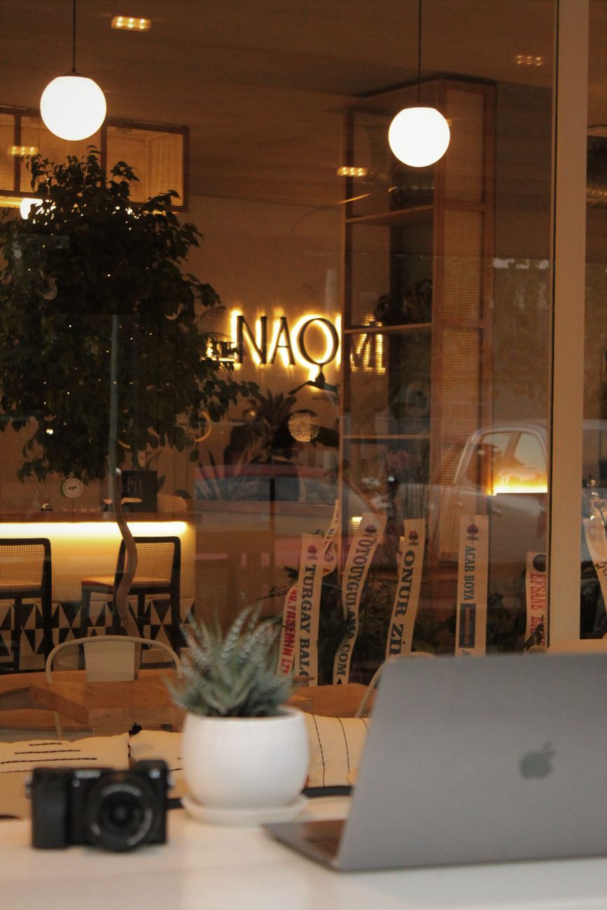 A stylish workspace in a cafe with a laptop, camera, and potted plant on a modern table.