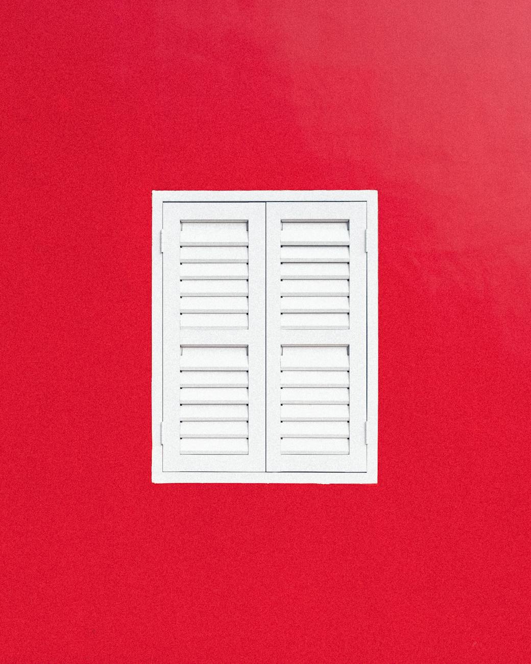 A minimalist white shuttered window centered on a vibrant red wall, Singapore.