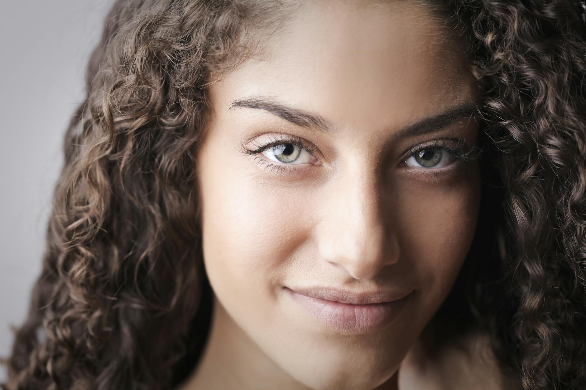 Close-up portrait of a smiling young woman with curly hair and beautiful eyes.