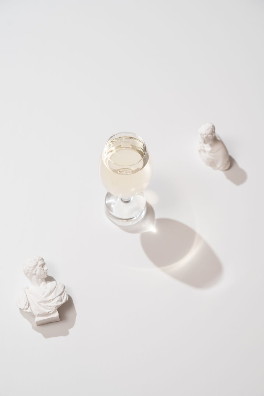 A glass of champagne surrounded by elegant marble busts on a clean white background.