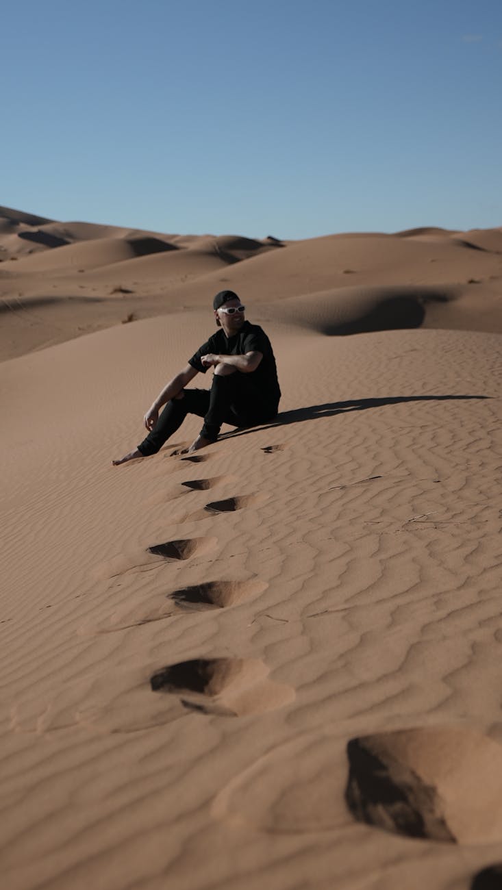 Person sitting on sand dunes in Merzouga desert, Morocco, showcasing isolation and adventure.
