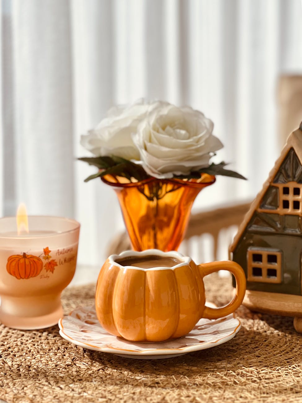 Warm autumn scene featuring a pumpkin-shaped mug, candle, and white rose centerpiece.
