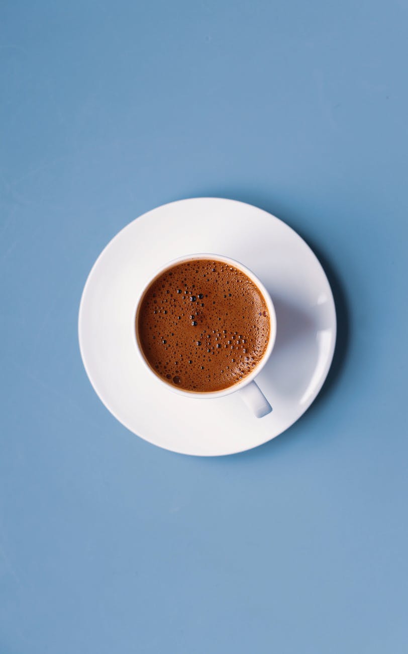 A delicate cup of Italian espresso on a white saucer set against a serene blue background.
