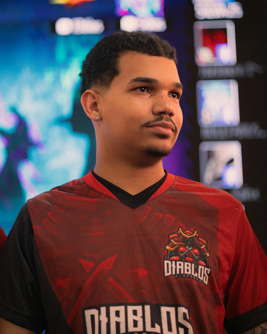 A team member in an e-sports event wearing a Diablos jersey with colorful screens in the background.