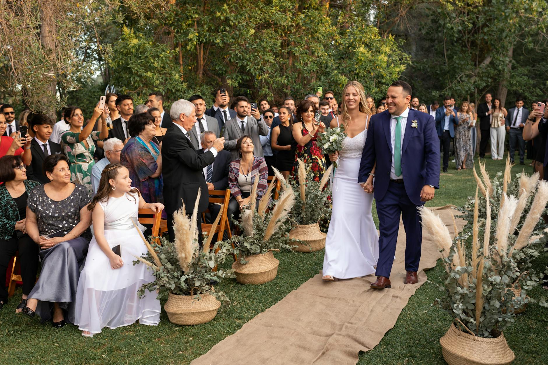 A happy wedding couple walks down the aisle outdoors in Mendoza, Argentina, surrounded by guests.
