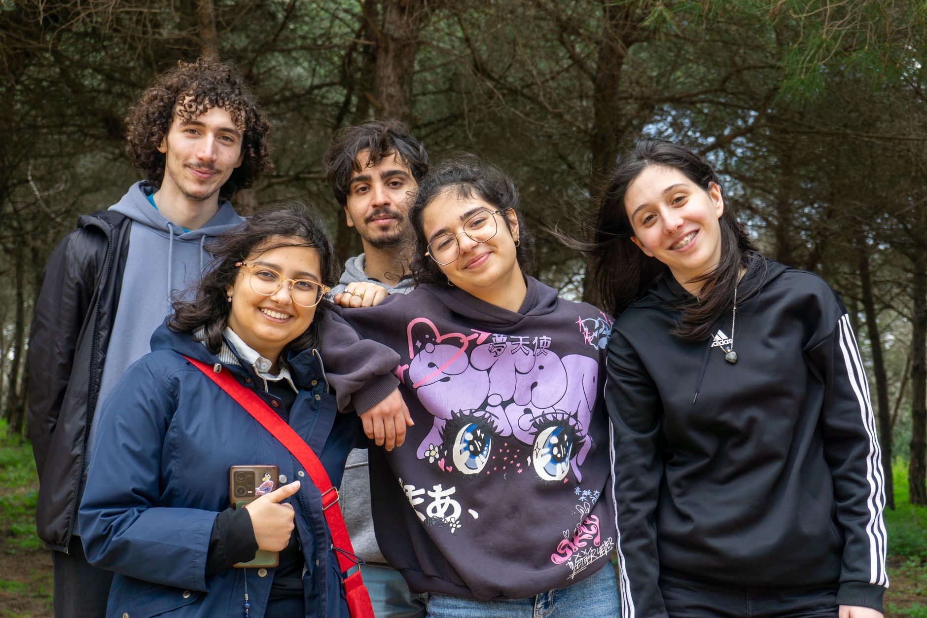 A joyful group of young adults smiling together in a serene forest setting, enjoying a day outdoors.