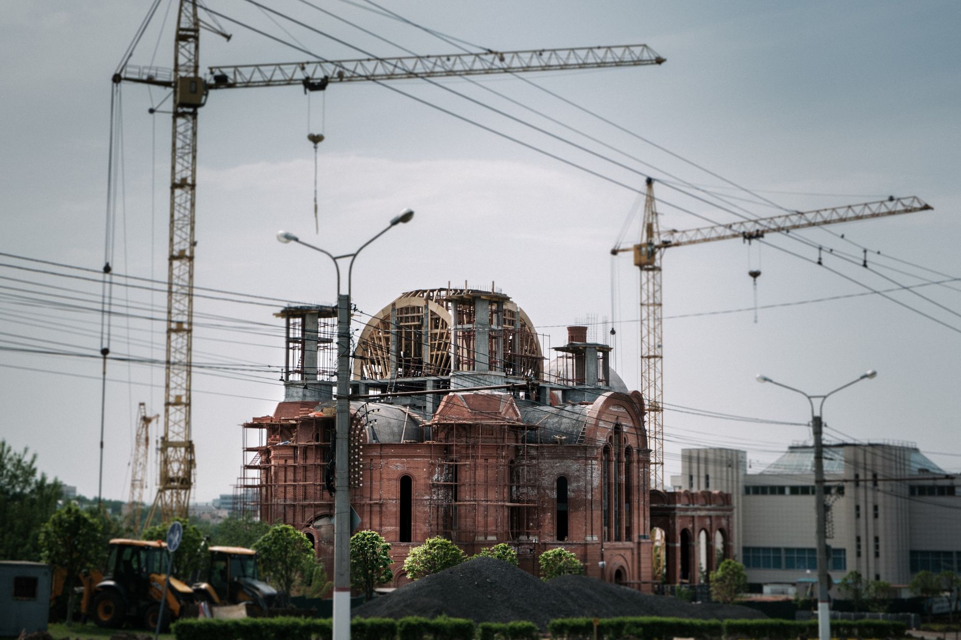 A city scene of a red brick building under construction with visible cranes.