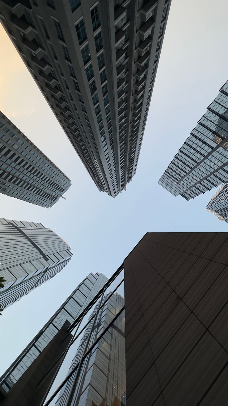 Dramatic view of towering modern skyscrapers from below against a soft sky.