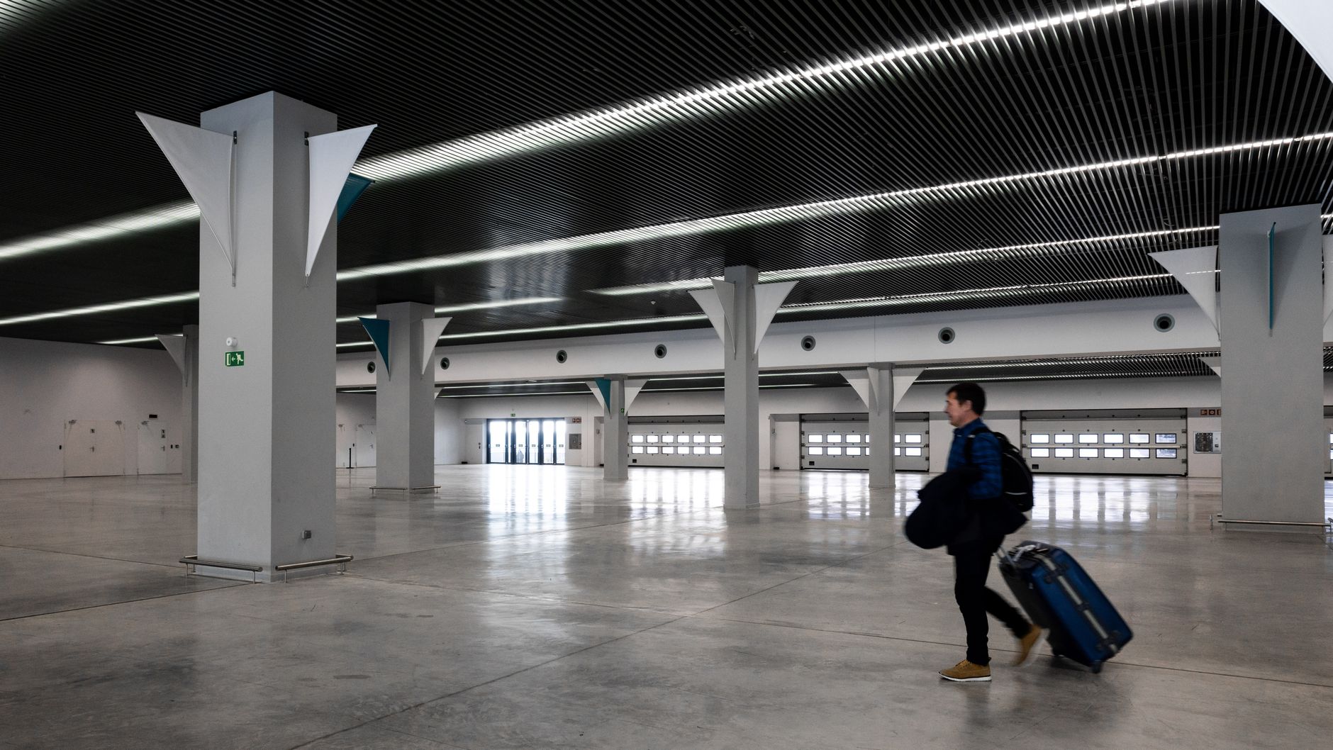 A man with luggage walking through a spacious, modern, empty airport hall.