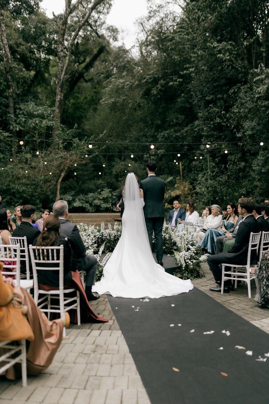 Bride and groom walk down the aisle in a lush forest setting with guests seated.