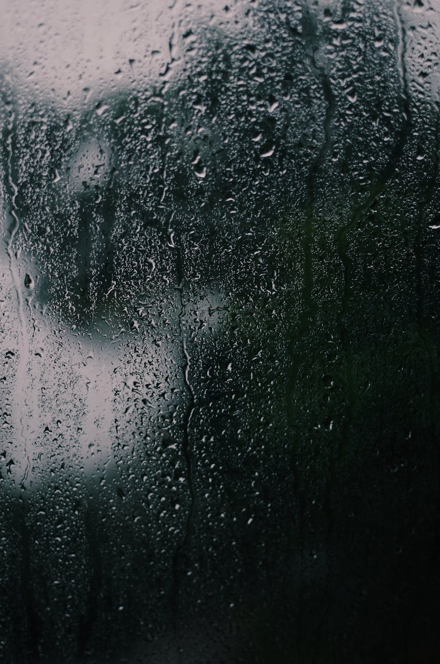 A dark and textured close-up of rain on a glass surface, capturing reflections and moodiness.