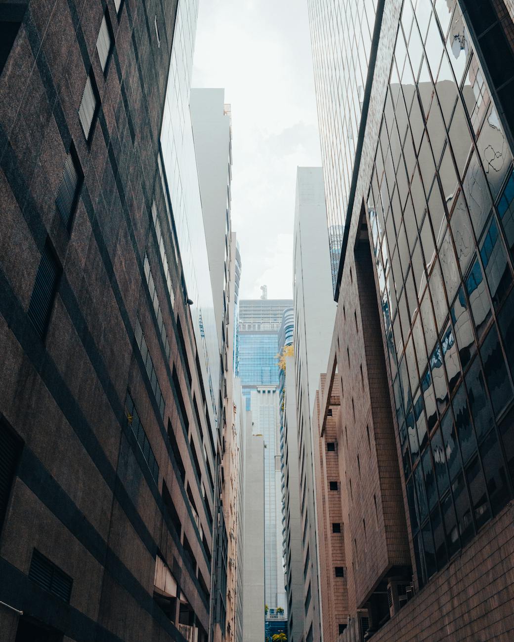 Low angle shot of Singapore skyscrapers with reflective facades in a narrow alley, showcasing modern architecture.