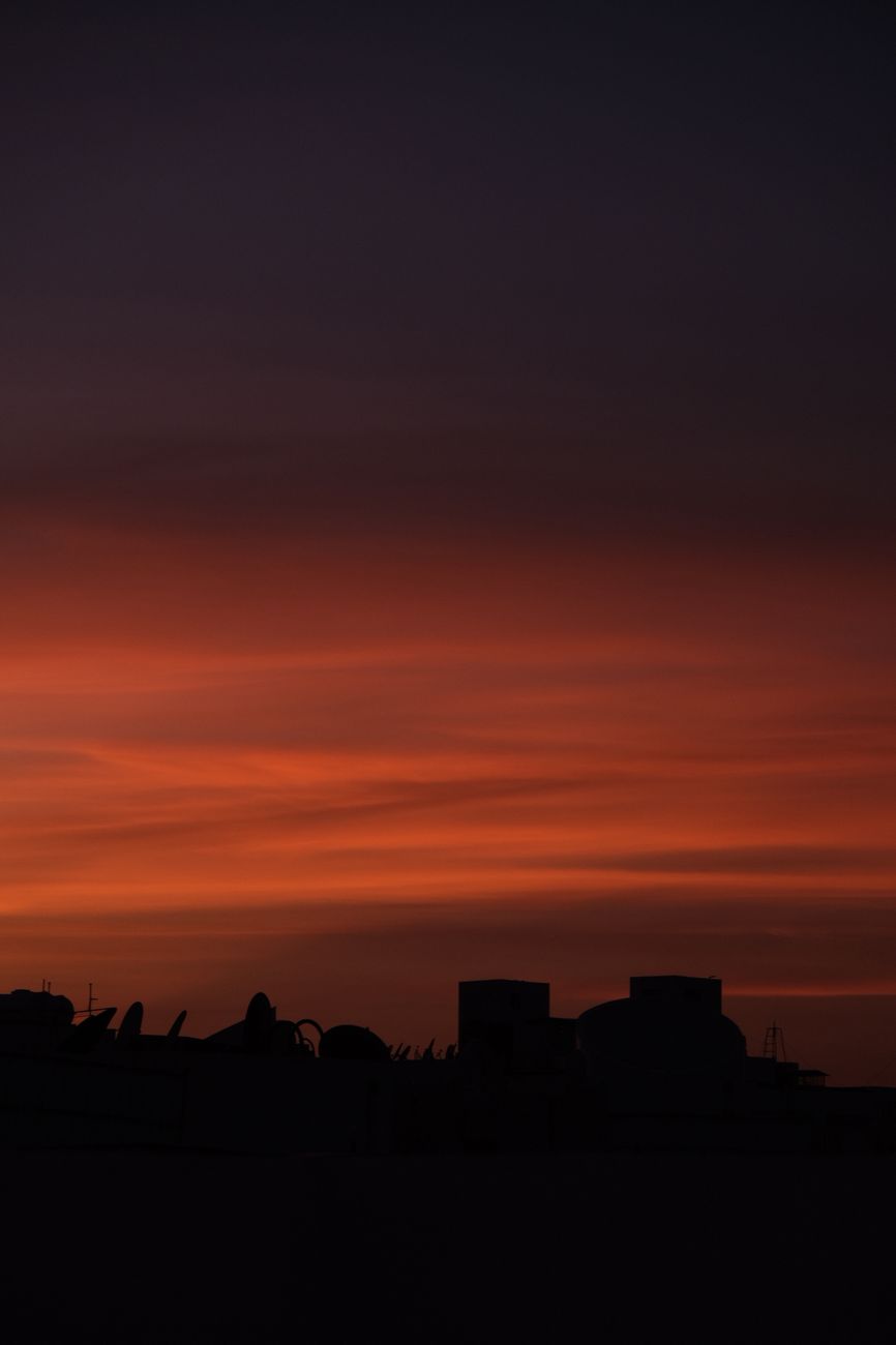 Silhouette of buildings at sunset, featuring vibrant orange and purple hues in the sky.