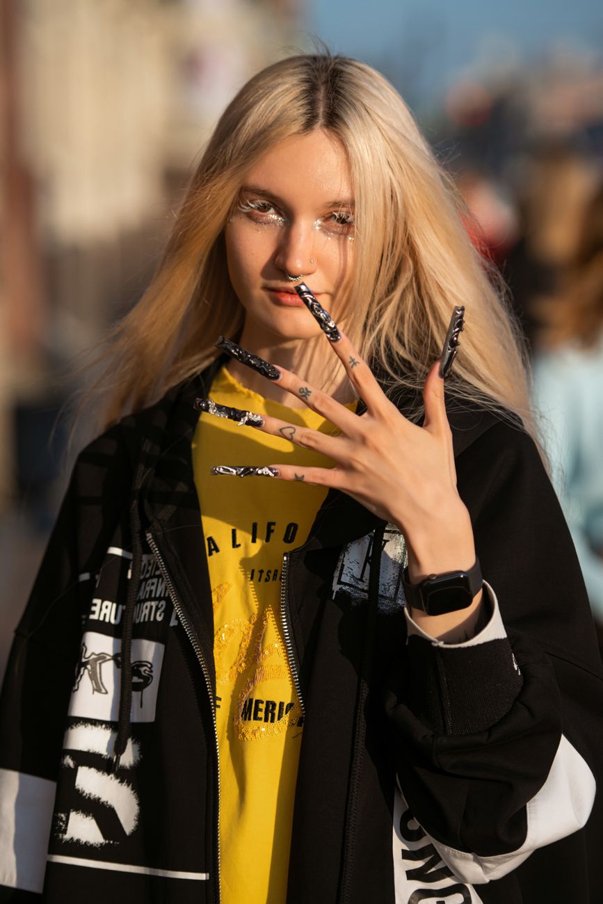 Chic urban street fashion featuring a young blonde woman with trendy acrylic nails, highlighting modern style and attitude.