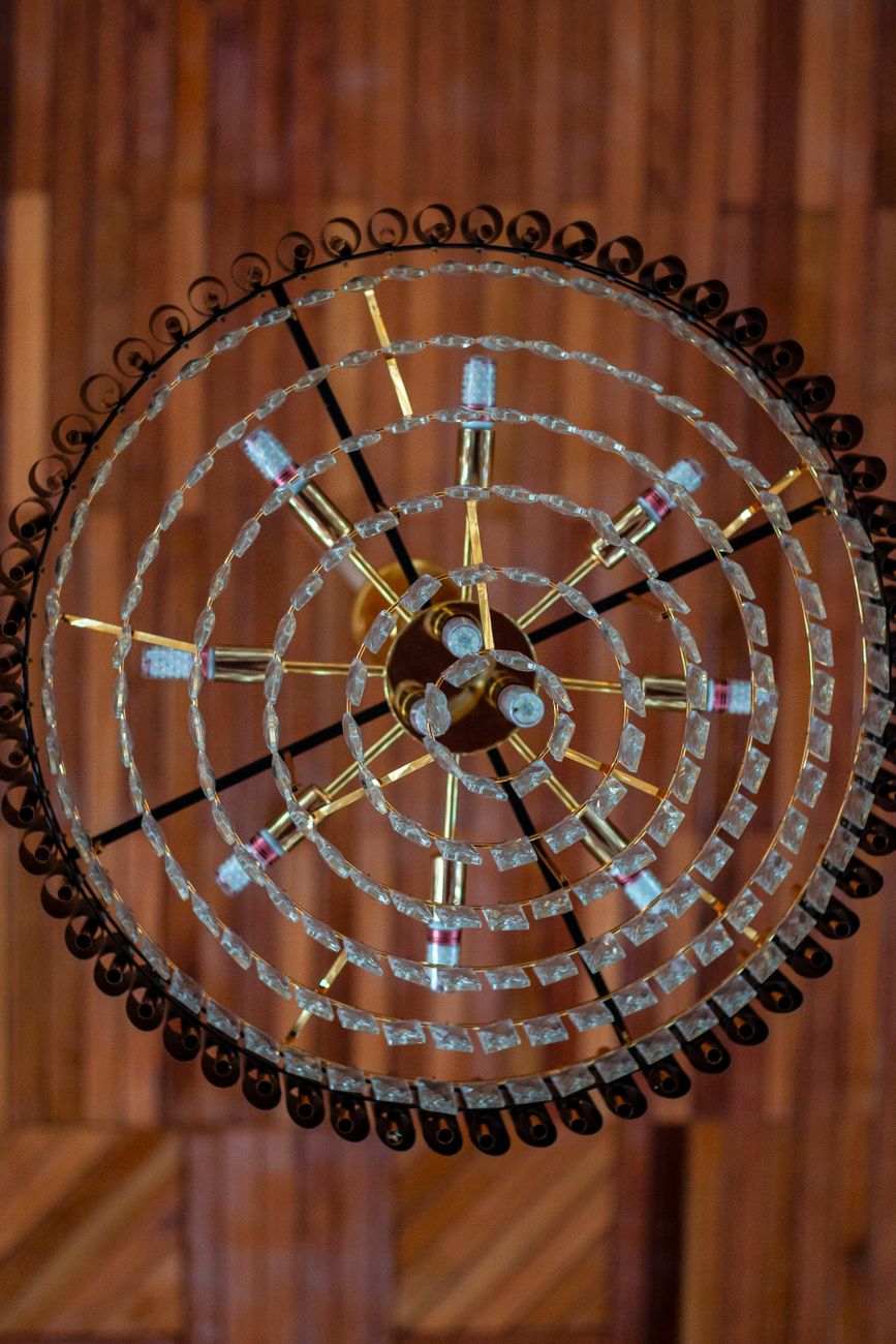 Top-down view of a vintage glass chandelier with intricate design features against a wooden ceiling.