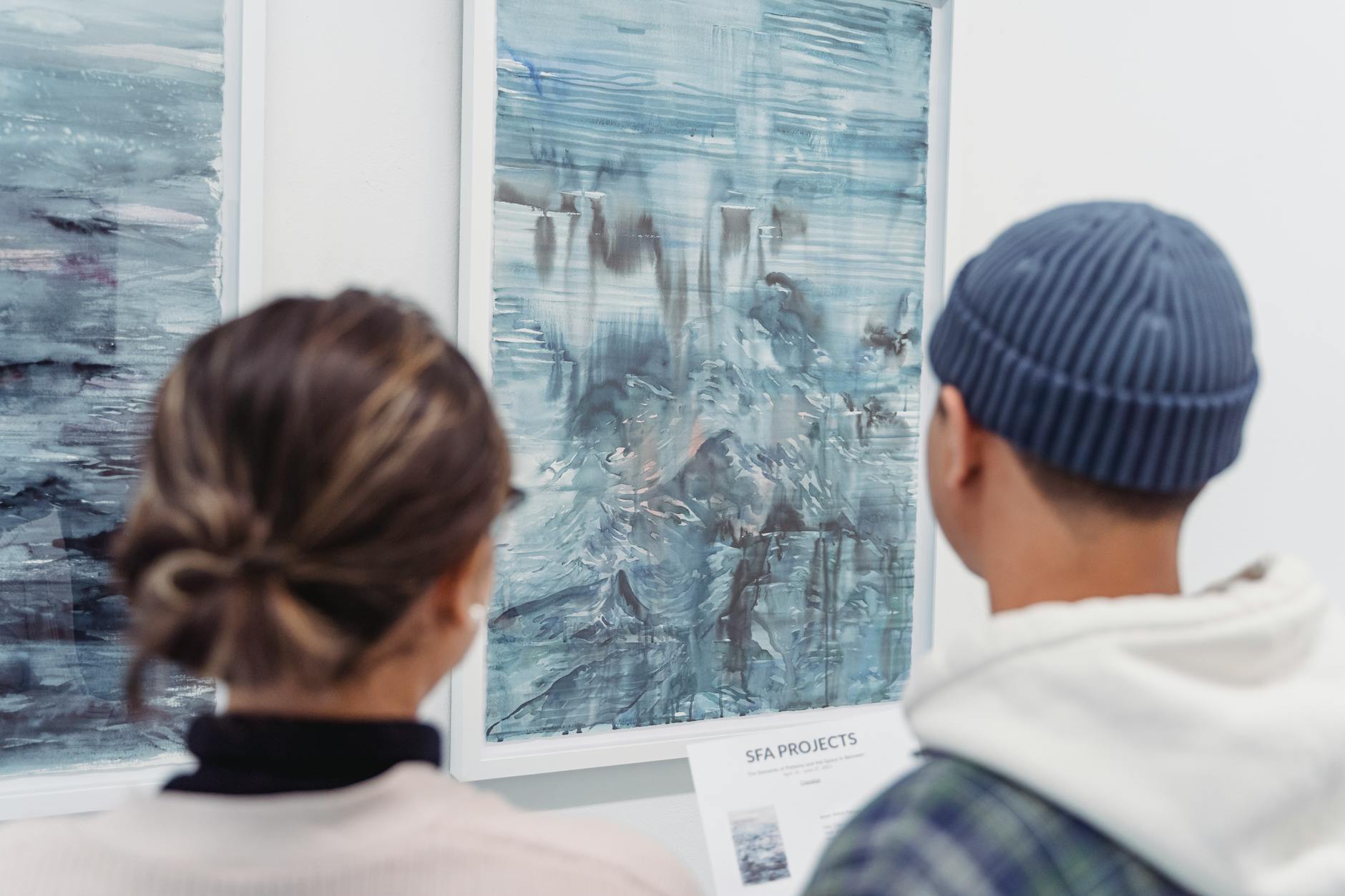 Visitors admire abstract paintings in an art gallery, showcasing modern artistic expressions.