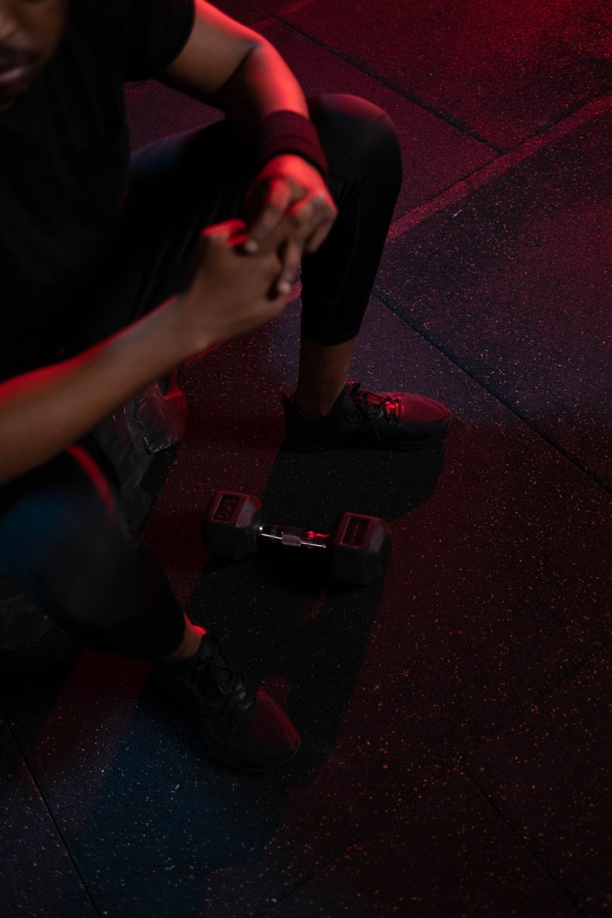 High-angle view of a man resting in a gym beside a dumbbell under red lighting.
