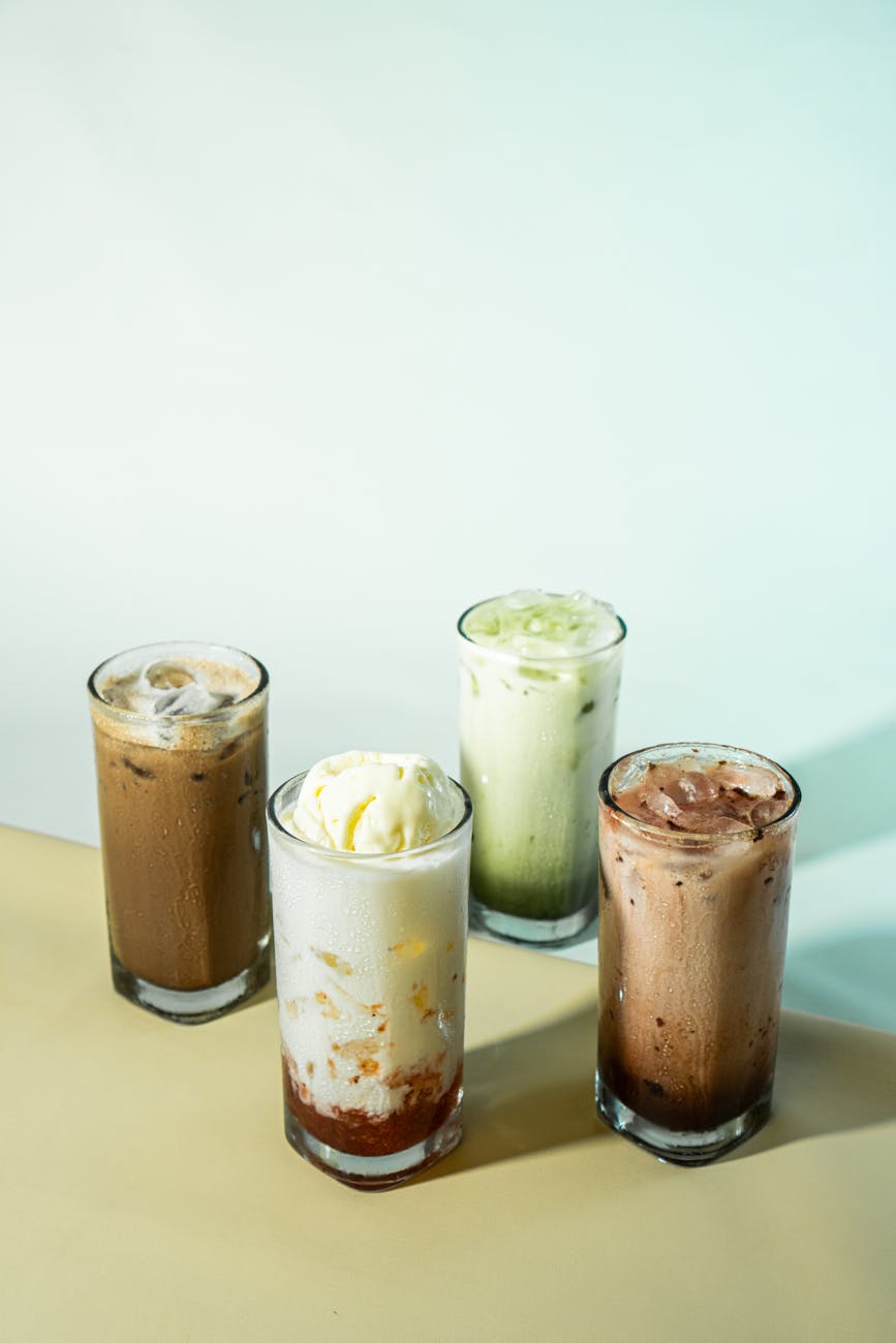 A selection of four iced drinks with creamy toppings in a minimalistic setting, perfect for refreshment.
