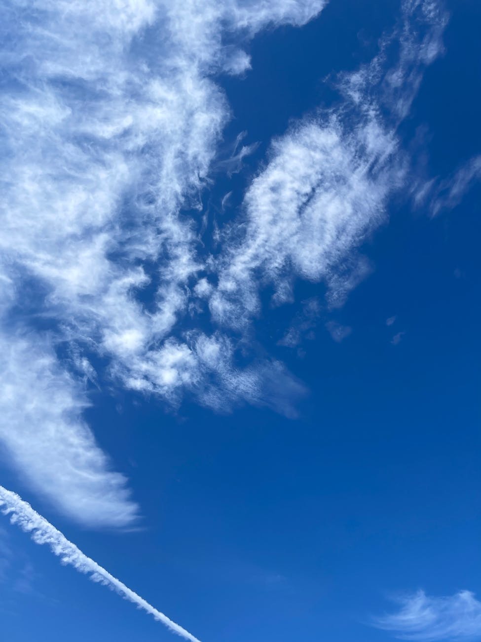 Clear blue sky in Dubai with wispy white clouds and a vapor trail, offering serene visuals.