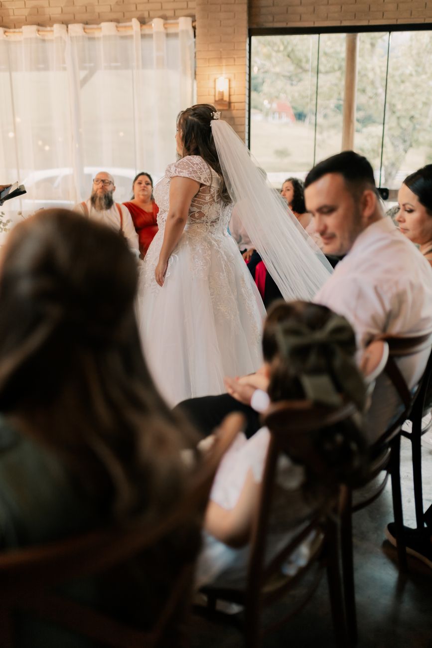 Bride in white dress speaks to seated guests at elegant indoor wedding venue.