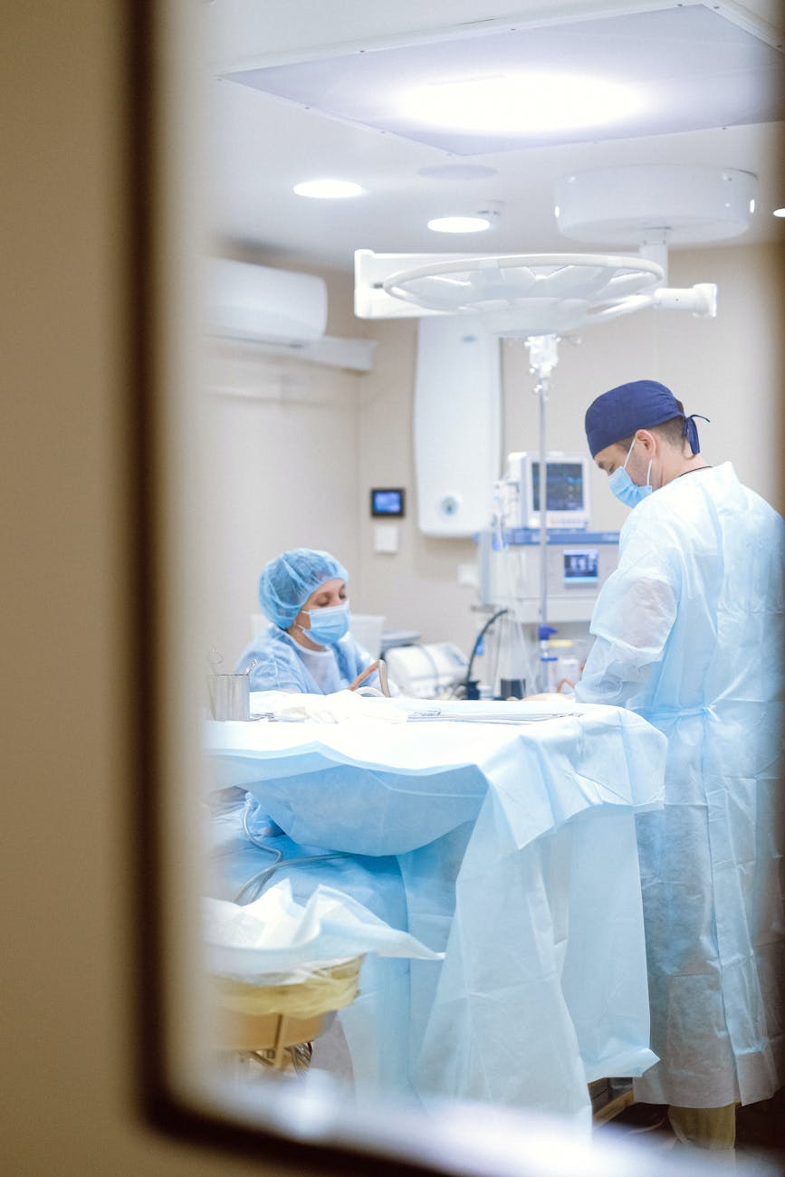 Medical professionals in surgical attire performing an operation in a sterile hospital environment.