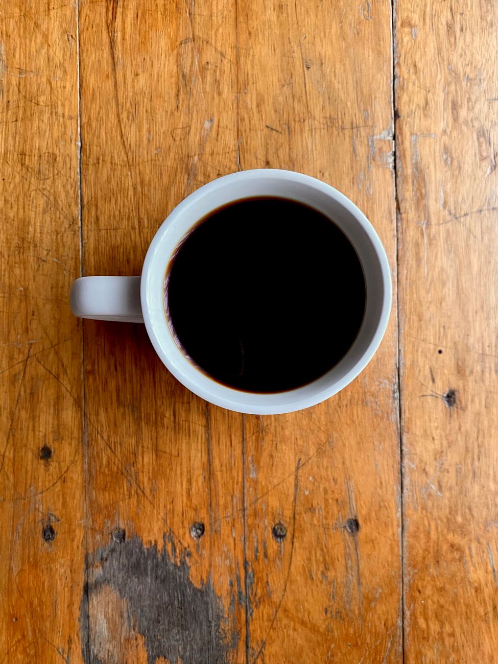 A simple white mug filled with black coffee on a rustic wooden table.