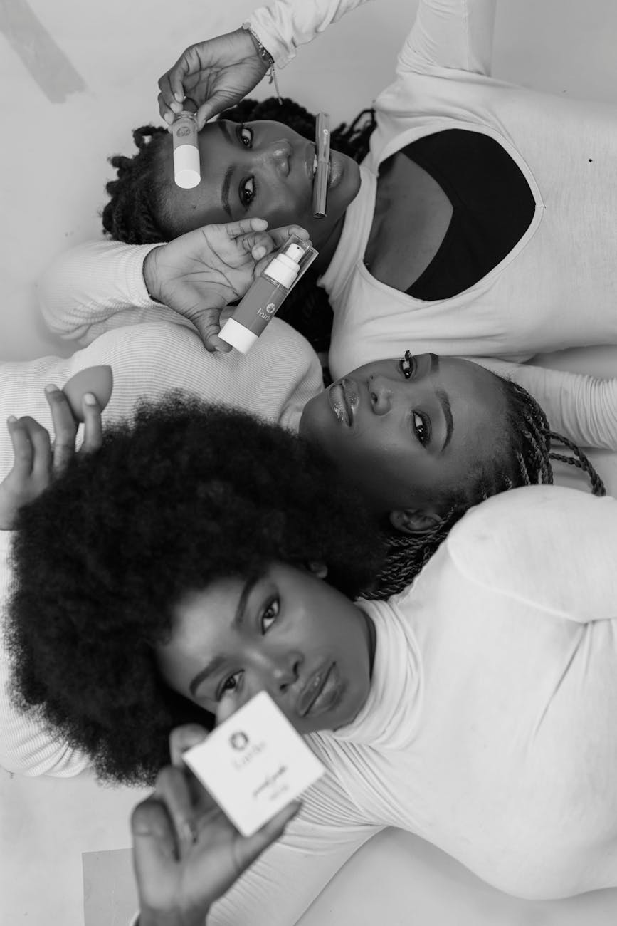Black and white portrait of three women holding skincare and beauty products in a graceful pose.